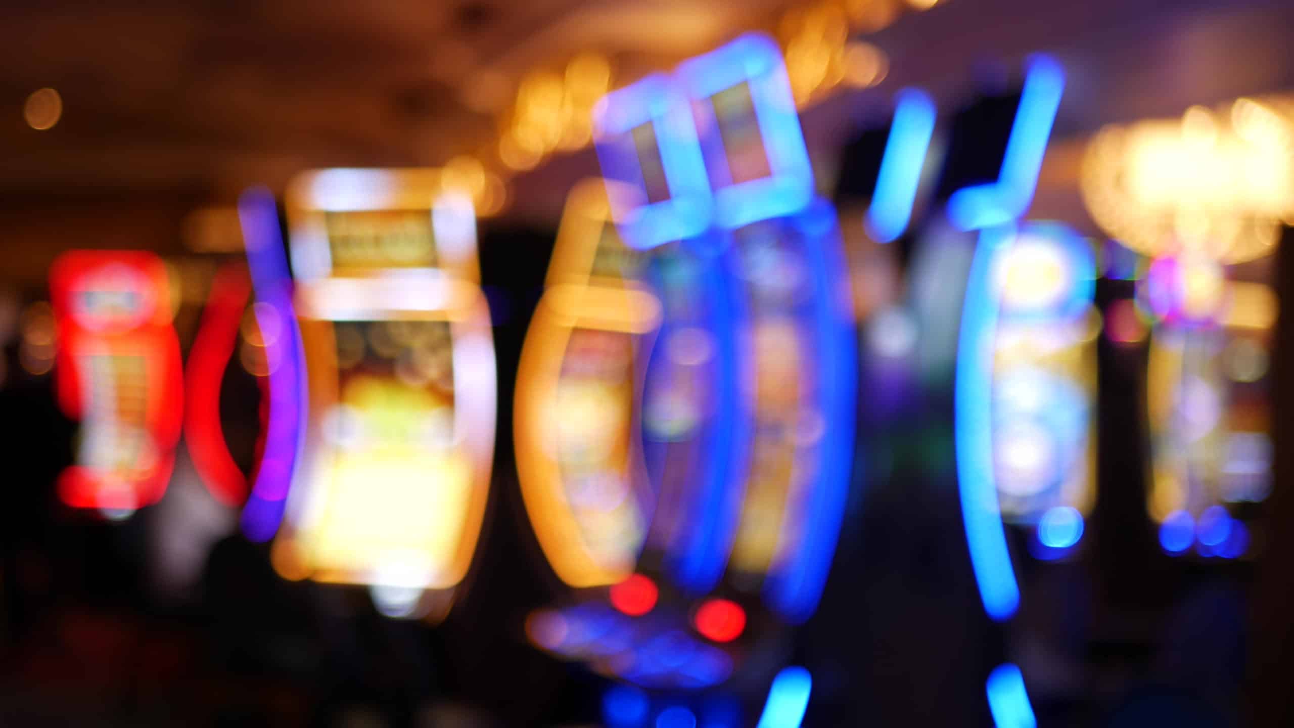 Blurred view of colorful illuminated gaming machines in blue, red, and gold tones with warm dim ambient lighting